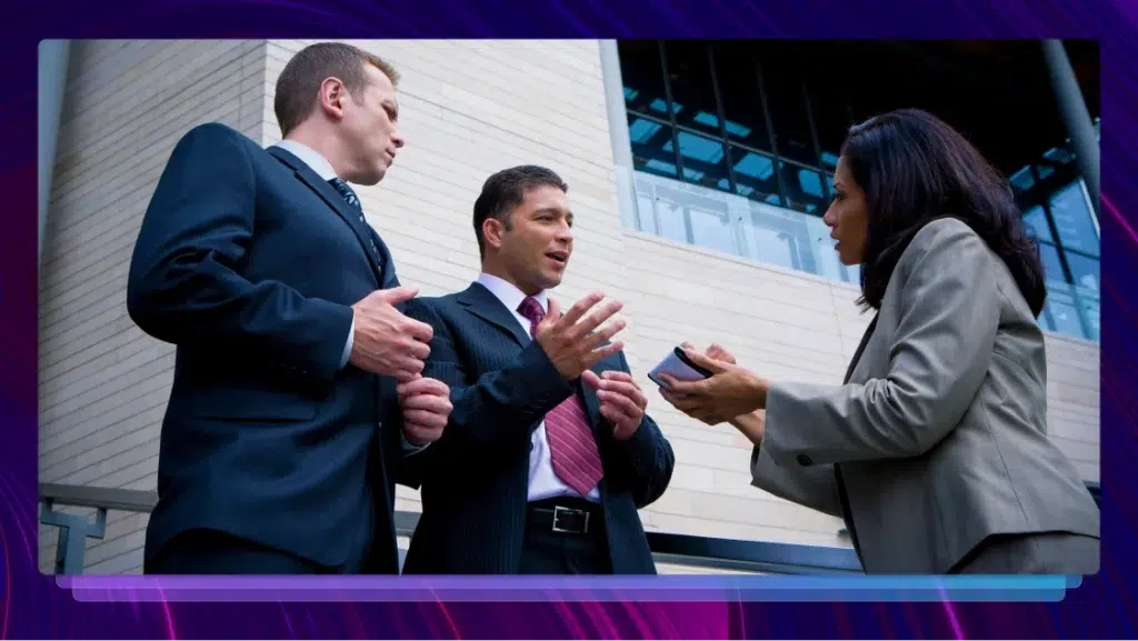 Two attorneys in suits talking to a court reporter in front of a courthouse.