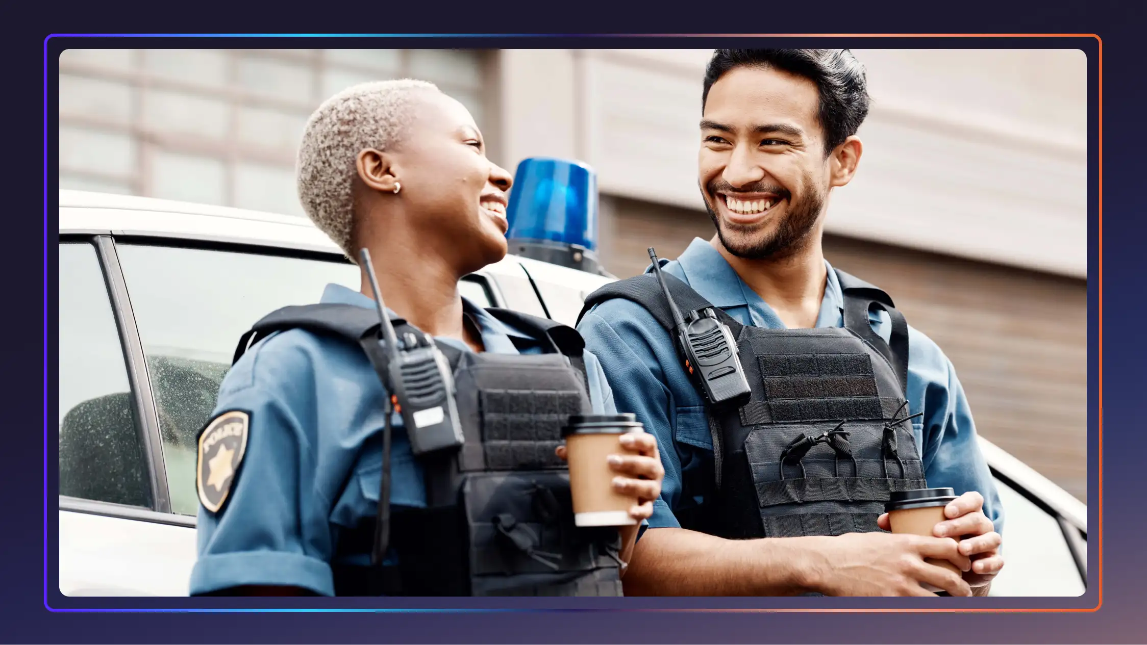 A female and male police officer stand together in uniform, laughing and smiling.